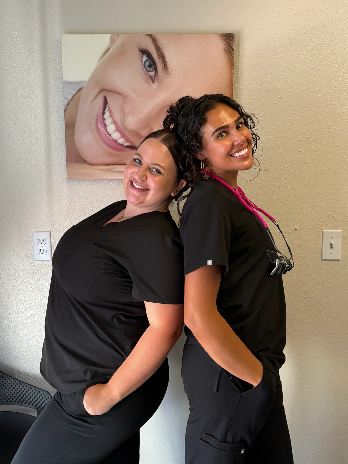 Two Mesa Dental Group team members smiling back-to-back in the office
